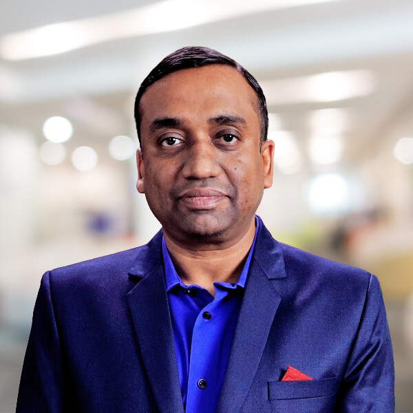 Professional headshot: man in a navy blue suit and blue shirt, bright office background, neutral expression.